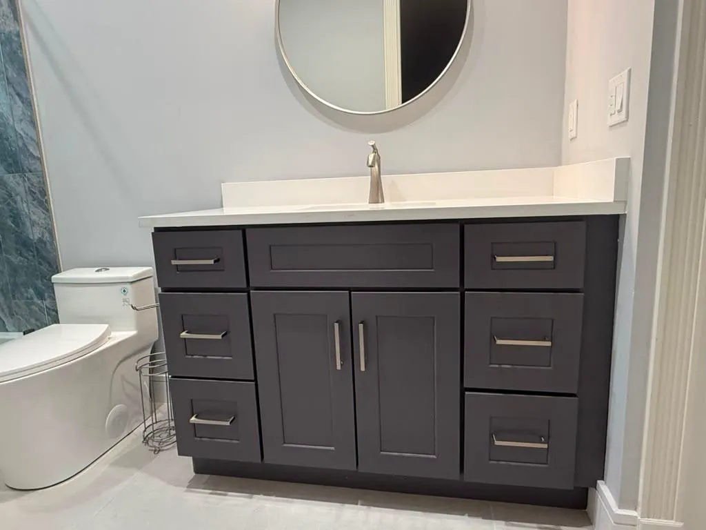 Installed charcoal shaker vanity with white countertop and round mirror