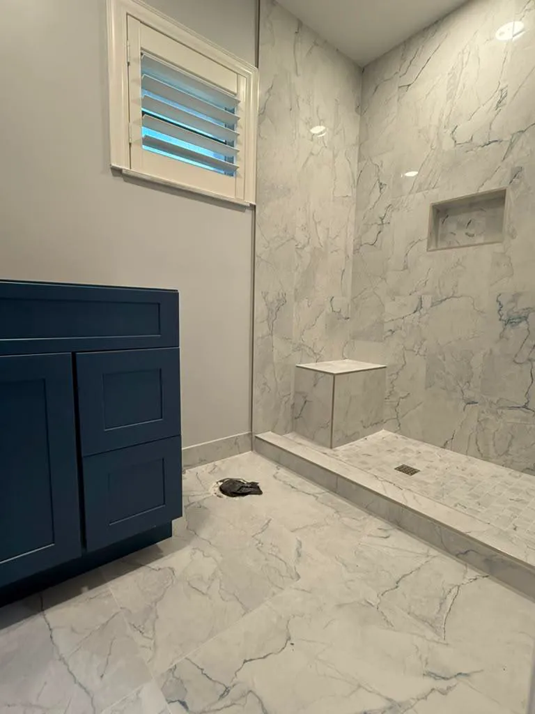 Completed walk-in shower with blue-veined marble-look tile, bench, niche, and navy vanity