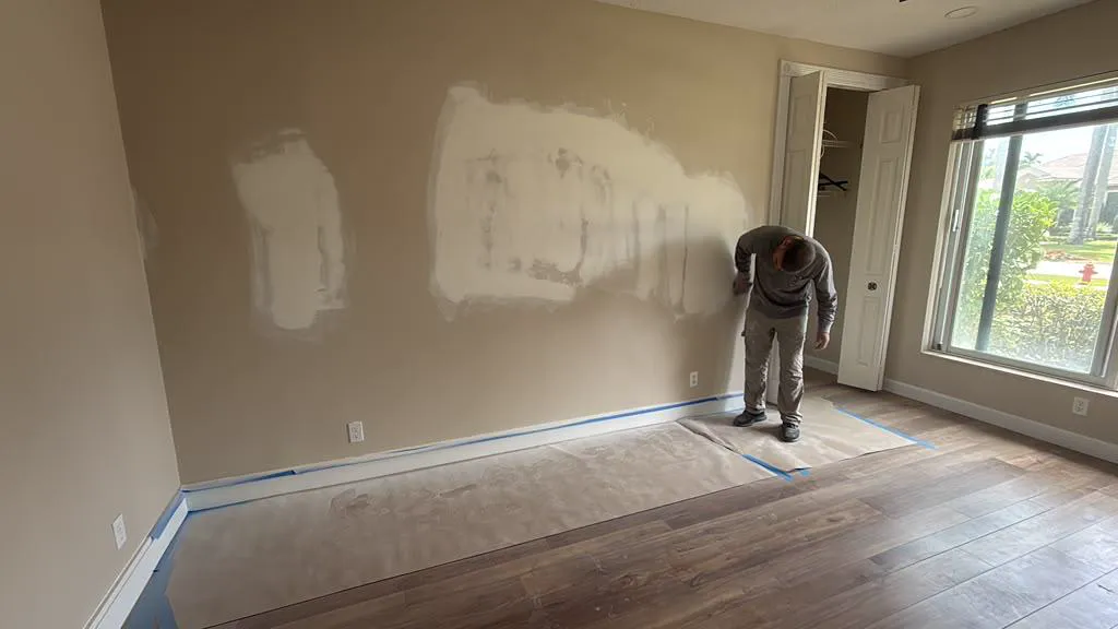 Painter skim-coating and preparing walls with floors protected