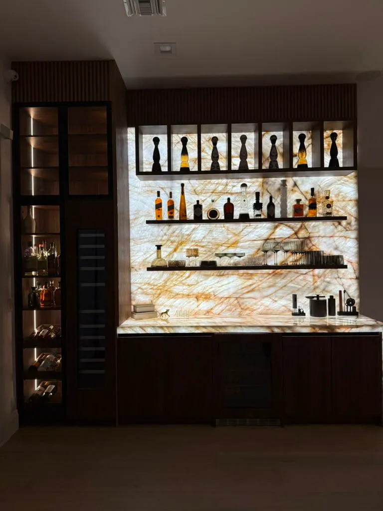 Custom home bar with backlit onyx-look wall, display shelving, and wine refrigeration